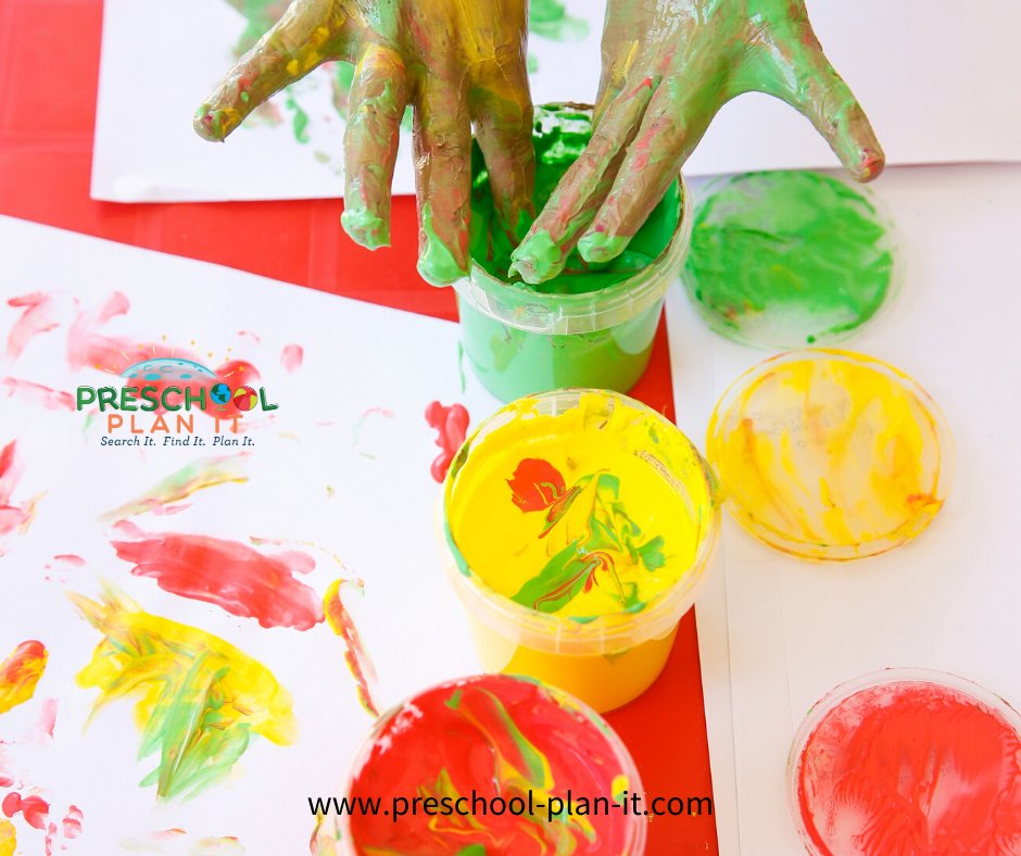 Hands fingerpainting with green paint on paper in a preschool art interest center.